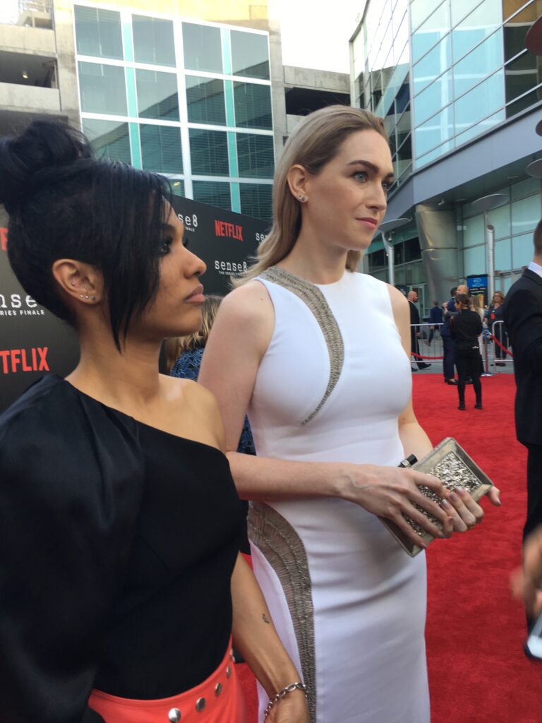 a black woman with black hair, wearing a black top and red skirt, standing next to a white woman with blond hair wearing a white dress on the red carpet