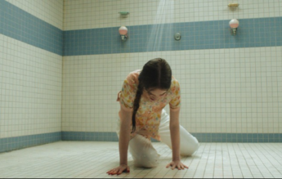 a young white girl with brown hair in a braid, wearing a flowery shirt and white pants, on her hands and knees in a gym shower