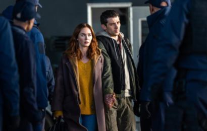 Disclosure Day Review - a white woman wearing a yellow sweater, jeans, and a long brown coat holds the hand of a white man wearing brown pants and a hoodie, surrounded by several men in blue suits