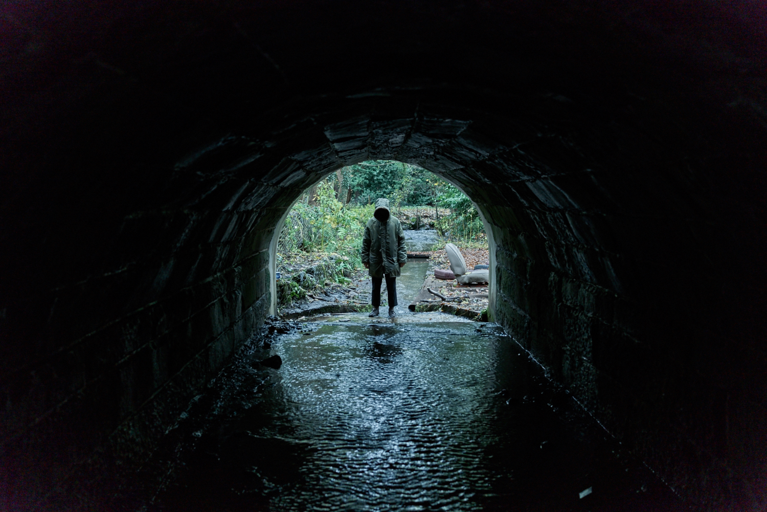 a hooded man at the edge of a tunnel over a water way