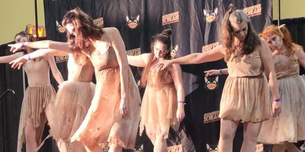 a group of dancers, dressed in bloody shabby clothes, reach to the left, heads down