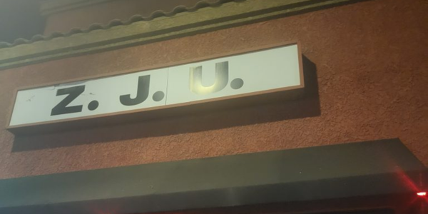 The outside of a store front, posters aligning the walls. A sign at the top states 'Z. J. U.'