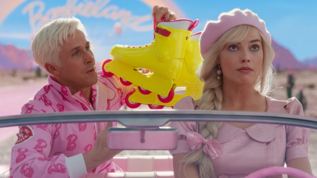 A bleached blond man (Ryan Gosling as Ken) holds up a pair of plastic yellow roller blades, while a blond woman (Margot Robbie as Barbie) sighs. The two sit in a car