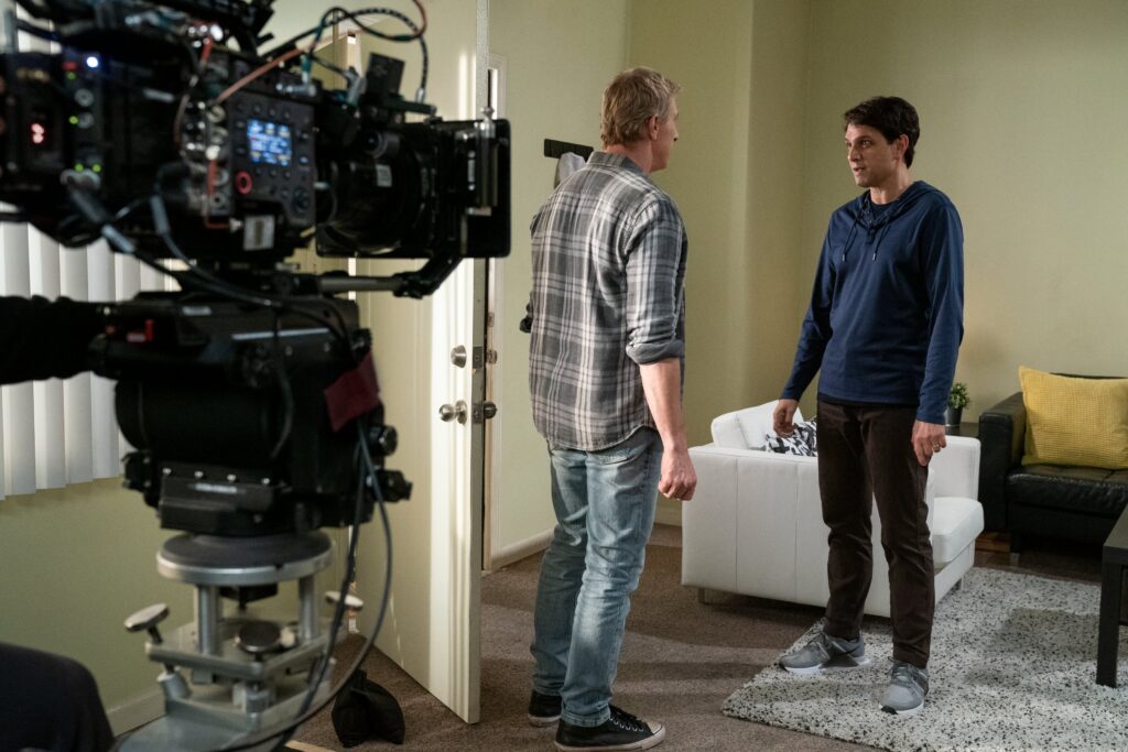 a behind the scenes photo: a capera is on two men in an apartment